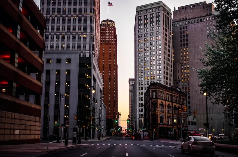 A downtown Detroit street at dusk, warm light in the gap between towers.